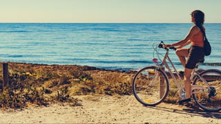 Woman riding bicycle outdoor on beach. Holidays, sport and recreation