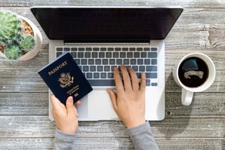 Person Holding An American Passport While Using A Laptop Computer